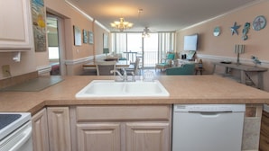 A modern kitchen with a central island, a dishwasher, and a dining area with a view. - Beautiful Ocean Front 3 Bedroom Condo (Murrells Inlet)