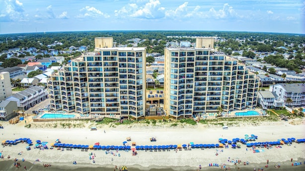 A beachfront hotel with multiple high-rise buildings, a sandy beach, and a pool area. - Surfmaster 909 - One-bedroom, one-and-a-half-bath oceanfront condo with pools (Garden City Beach)