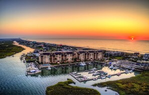 Uma marina com barcos atracados, um edifício à beira-mar e um pôr do sol sobre o oceano.