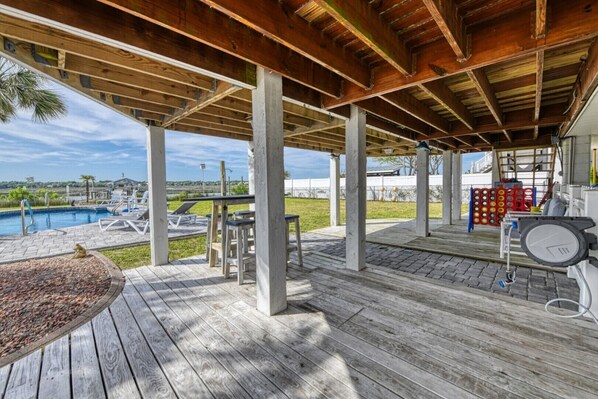 A covered outdoor area with a pool, wooden deck, and seating.