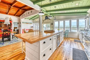 A spacious kitchen with a large island, wooden flooring, and a view of the outdoors through large windows.