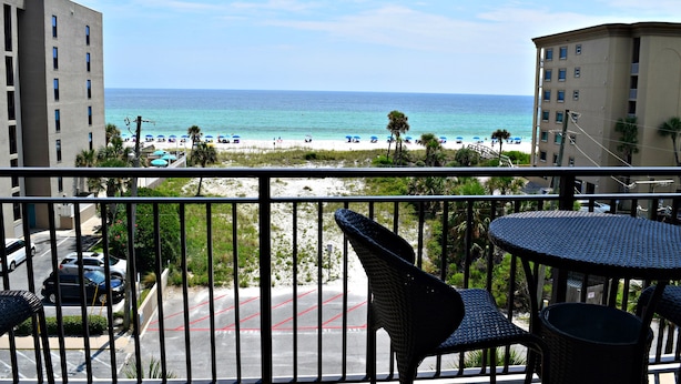 A balcony with a view of the beach, a parking area, and a building with a flat facade.
