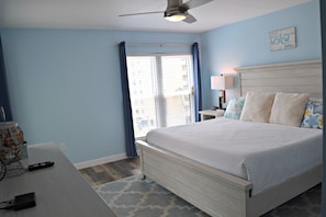 A bedroom with a bed, a desk, a lamp, and a ceiling fan.