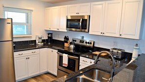 A modern kitchen with white cabinets, stainless steel appliances, a double sink, and a window with blinds.