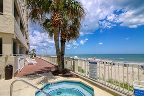 A pool area with a palm tree, a beach view, and a caution sign.