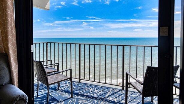Un balcone con vista sull'oceano, dotato di due poltrone in vimini e un tappeto decorato.