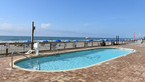 Una piscina con vista sull'oceano, un pontile in legno e una recinzione con ombrelloni.