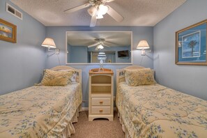 A bedroom with two single beds, a dresser, a mirror, and a ceiling fan.