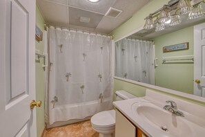 A bathroom with a toilet, sink, and shower curtain with palm tree patterns.