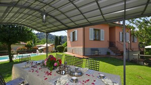 An outdoor dining area with a table set for a meal, surrounded by chairs, and a covered patio. - Villa Medicina (Pescia)