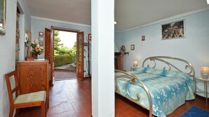 A room with a bed, a chair, a small table, and a door leading to an outdoor area. - Villa Medicina (Pescia)