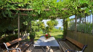 An outdoor seating area with a table and benches under a pergola, surrounded by greenery and a view of the landscape. - Villa Medicina (Pescia)