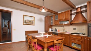 A kitchen with wooden cabinets, a dining table with chairs, and a hanging light fixture. - Villa Medicina (Pescia)