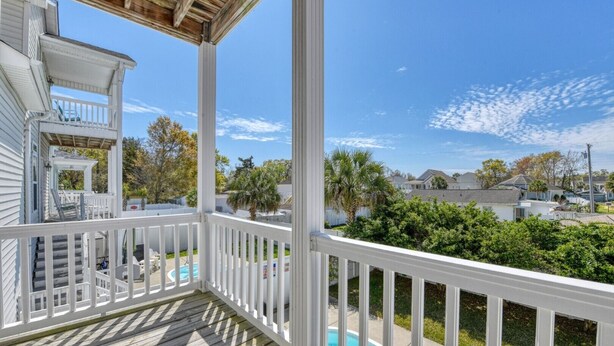 A covered porch with a pool, white railings, and a view of neighboring houses.