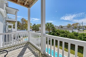 A covered porch with a pool, white railings, and a view of neighboring houses.