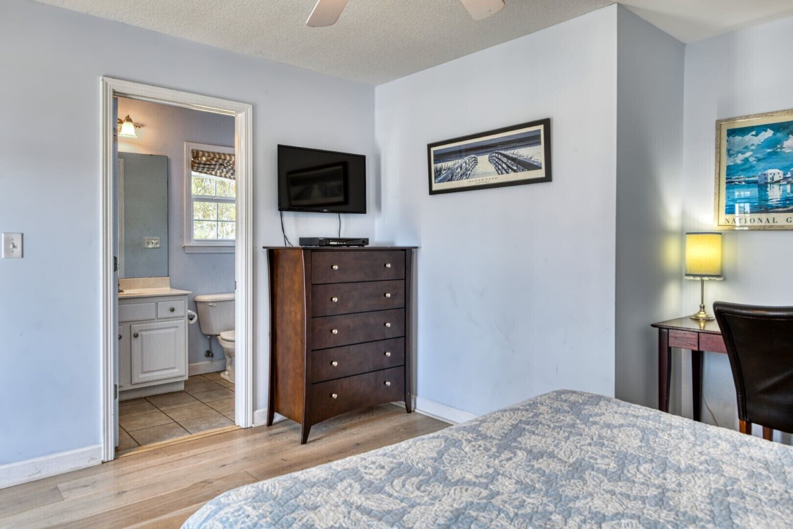 Een slaapkamer met een bed, een dressoir, een televisie, een lijst met een afbeelding en een lamp.