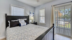A bedroom with a bed, nightstands, a ceiling fan, and a large window with a view of the outdoors.