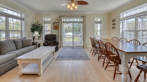 A spacious living room with a large wooden dining table, a leather sofa, and a ceiling fan.