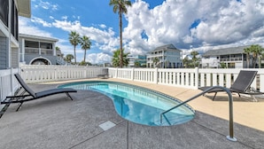 A swimming pool with lounge chairs, surrounded by a white fence, with houses and palm trees in the background. - Rucker Cottage - Crabbing & fishing off floating dock, private pool (Garden City Beach)