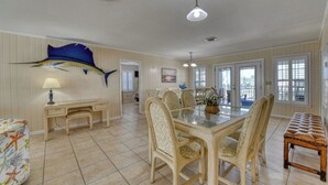 A spacious dining area with a large table and chairs, a decorative fish on the wall, and a view through the open door. - Rucker Cottage - Crabbing & fishing off floating dock, private pool (Garden City Beach)