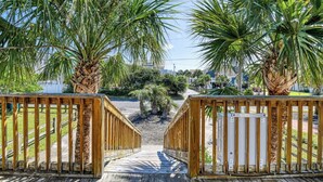 A wooden deck leading to a gated area with palm trees. - Rucker Cottage - Crabbing & fishing off floating dock, private pool (Garden City Beach)