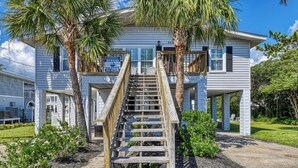 A two-story house with a wooden staircase leading to the front porch, surrounded by palm trees and a well-maintained lawn. - Rucker Cottage - Crabbing & fishing off floating dock, private pool (Garden City Beach)