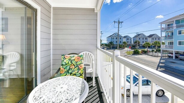 A balcony with a white railing, a round table, and a chair with a floral cushion.