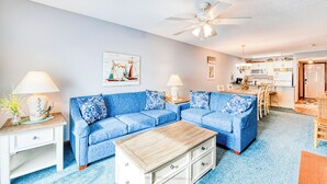 A living room with a blue sofa set, a wooden coffee table, and a ceiling fan. - Sandy Shores II 209 - Two-bedroom, two-bath oceanview condo in GCB (Garden City Beach)