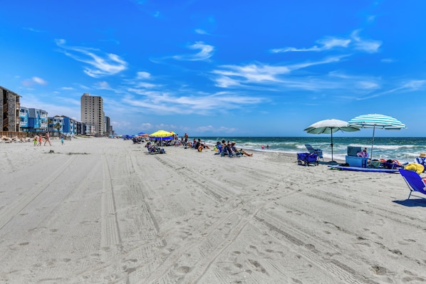 A beach with umbrellas, lounge chairs, and people.