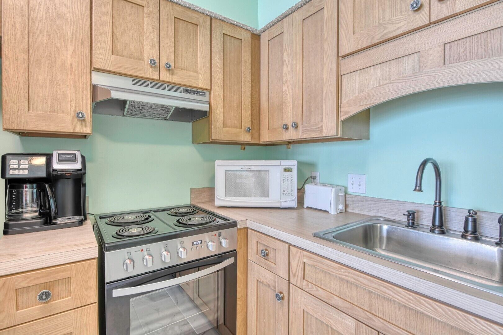 Una cocina con armarios de madera, estufa, microondas, cafetera y un lavabo.