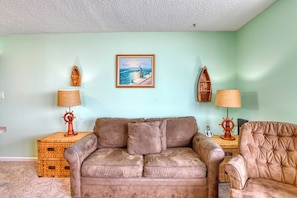 A living room with a brown leather sofa, a matching armchair, a wooden side table with a lamp, and a framed painting on the wall.