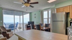 A kitchen with a refrigerator, a dining table with chairs, a ceiling fan, and a view of the ocean through large windows. - Sea Watch VIII 103 - Two Bedroom, One Bath Oceanfront Condo (Garden City Beach)