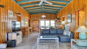 Un intérieur de chalet chaleureux, avec un revêtement mural en bois, un coin repas, un ensemble de canapés et un téléviseur.