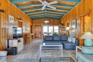Cozy cabin-style room with a high ceiling, seating area, dining table, and kitchenette.