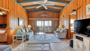 Un intérieur de chalet chaleureux avec des murs en bois, un ventilateur de plafond, une grande télévision et un balcon offrant une vue imprenable.