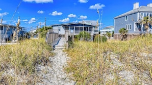 Une propriété située en bord de mer, avec une passerelle en bois menant à une maison dotée d’un porche.