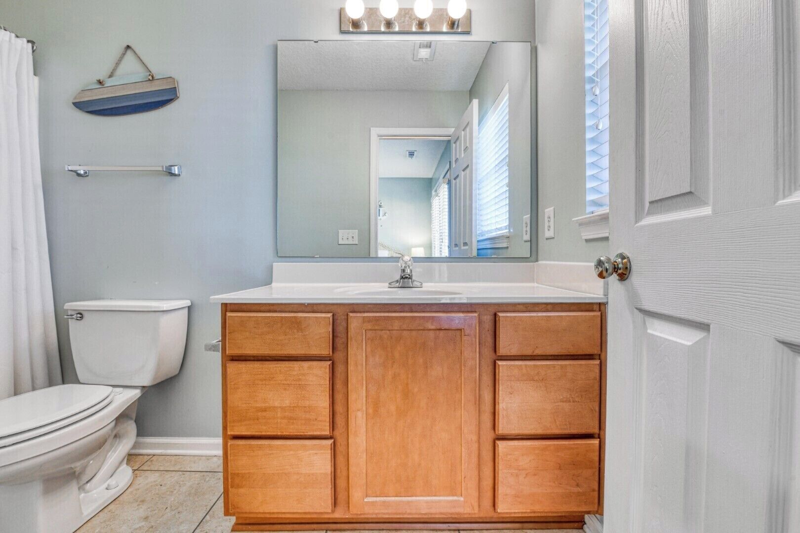 Ein Badezimmer mit einem Holzkosmetikschrank, einer weißen Toilette, einem Spiegel mit Beleuchtung und einem Handtuchhalter.