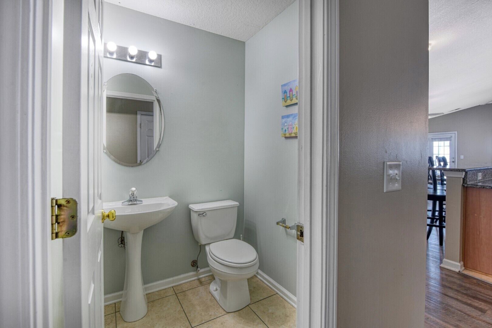 A bathroom with a pedestal sink, toilet, and a mirror with lights above.