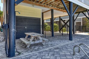 An outdoor patio area with a wooden table and benches, a covered seating area, and a black metal fence.