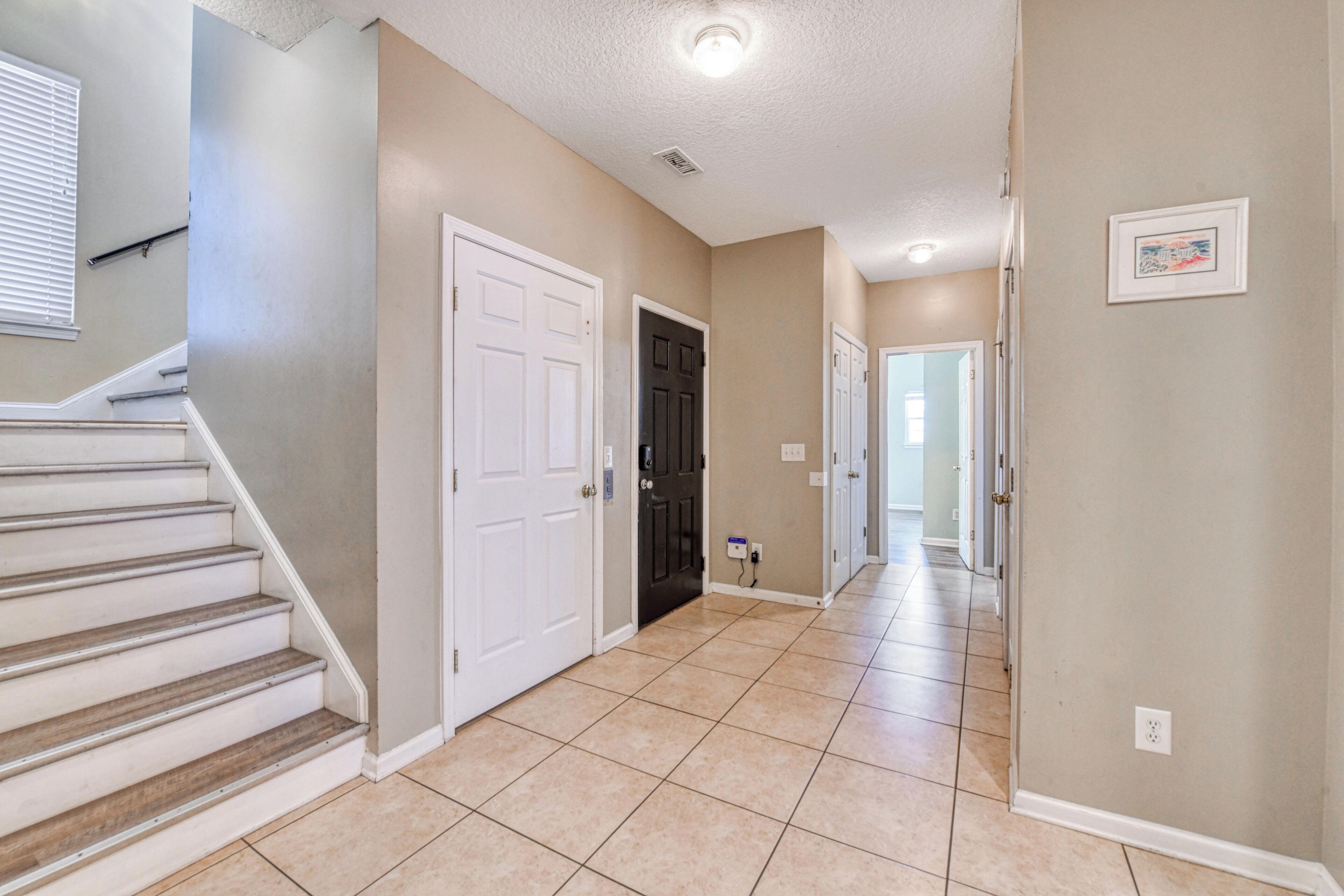A hallway with a staircase, doors, and a tiled floor.