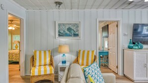 A living room with a sofa, two armchairs, a lamp, a painting, and a television. - Charming Coastal - 5 Bedroom, 4 Bath Beach House with Private Pool (Garden City Beach)