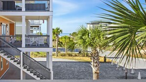 A multi-story building with balconies, a palm tree, and a view of the sea.