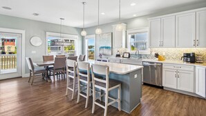 A modern kitchen with a central island, bar stools, pendant lights, and a dishwasher.