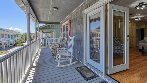 A covered porch with rocking chairs, a sliding glass door, and a view of a neighboring house. - Summer House - Clinkscales - Three-bedroom, two-bath beach house with Wi-Fi (Garden City Beach)