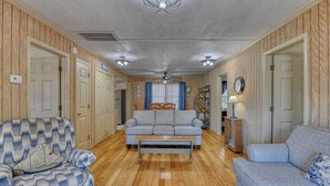 A living room with a sofa, a patterned armchair, a wooden floor, and a ceiling fan. - Summer House - Clinkscales - Three-bedroom, two-bath beach house with Wi-Fi (Garden City Beach)