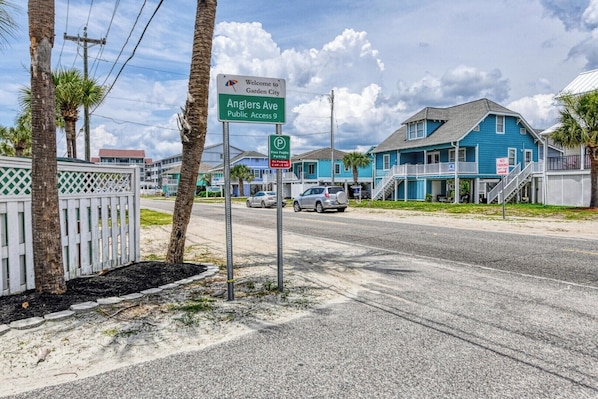 A street view with a sign for Anglers Ave Public Access 9, a blue building with a balcony, and a white fence.