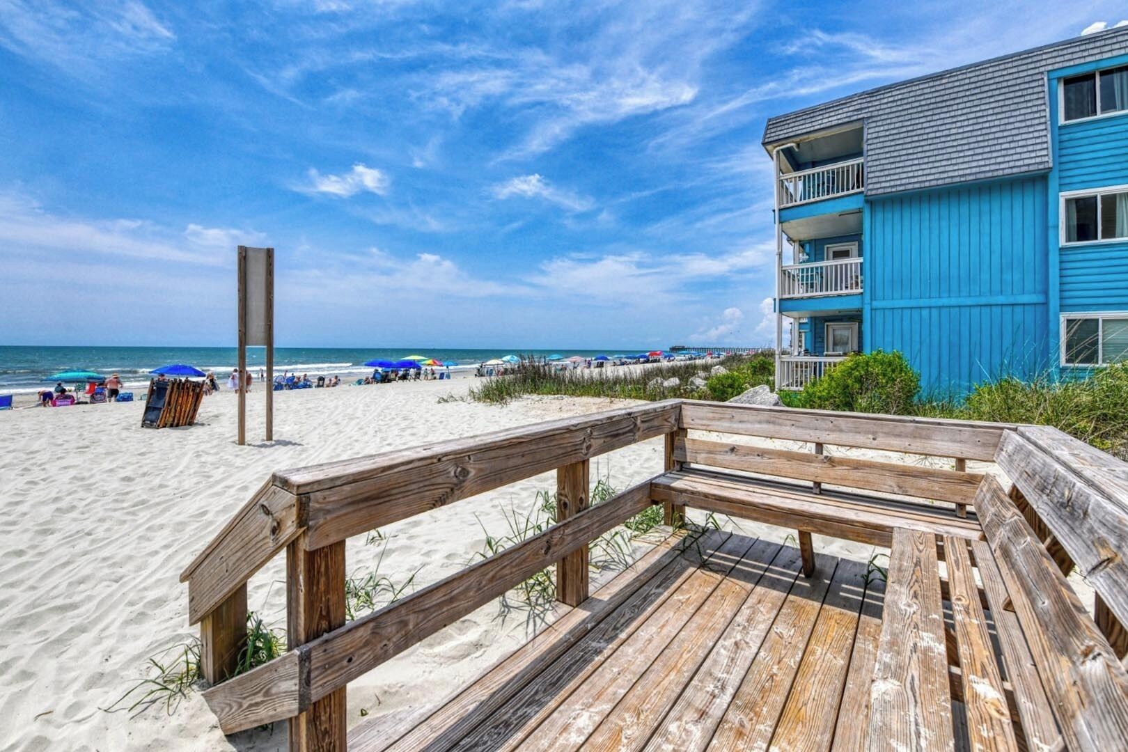 Una passerella in legno che conduce a una spiaggia, con un edificio blu sullo sfondo.