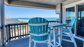 Un balcon avec vue sur l’océan, une table et deux chaises.
