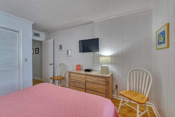 A bedroom with a bed, dresser, two chairs, a television, and a lamp.