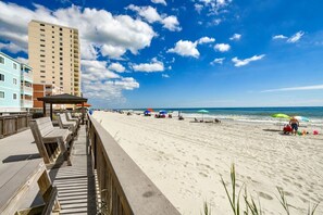 A beach with a wooden boardwalk, beach umbrellas, and a tall building in the background.